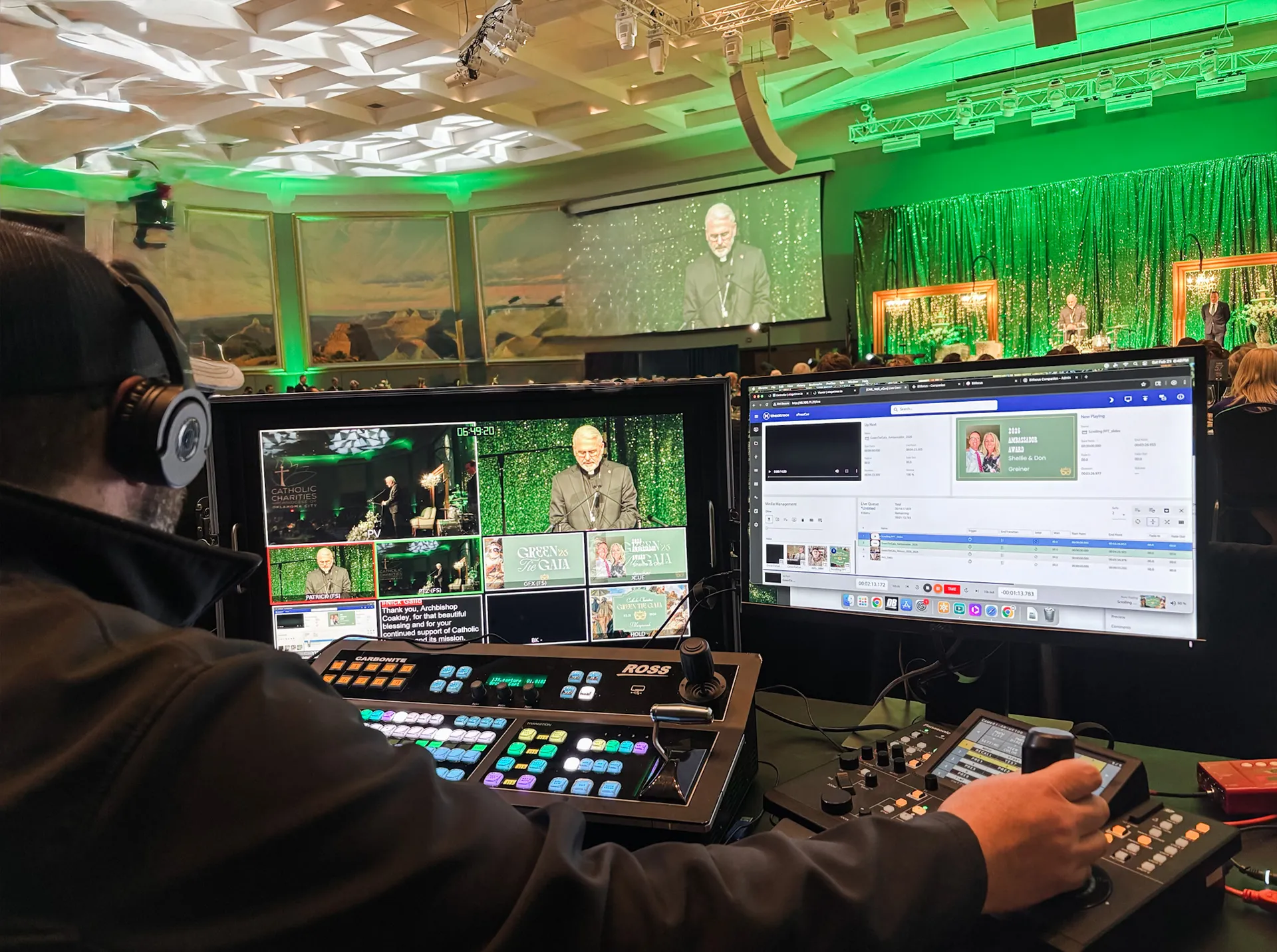 CNS video technician operating a multi-camera switcher board at the Green Tie Gala, with live feeds of the speaker and stage on screen