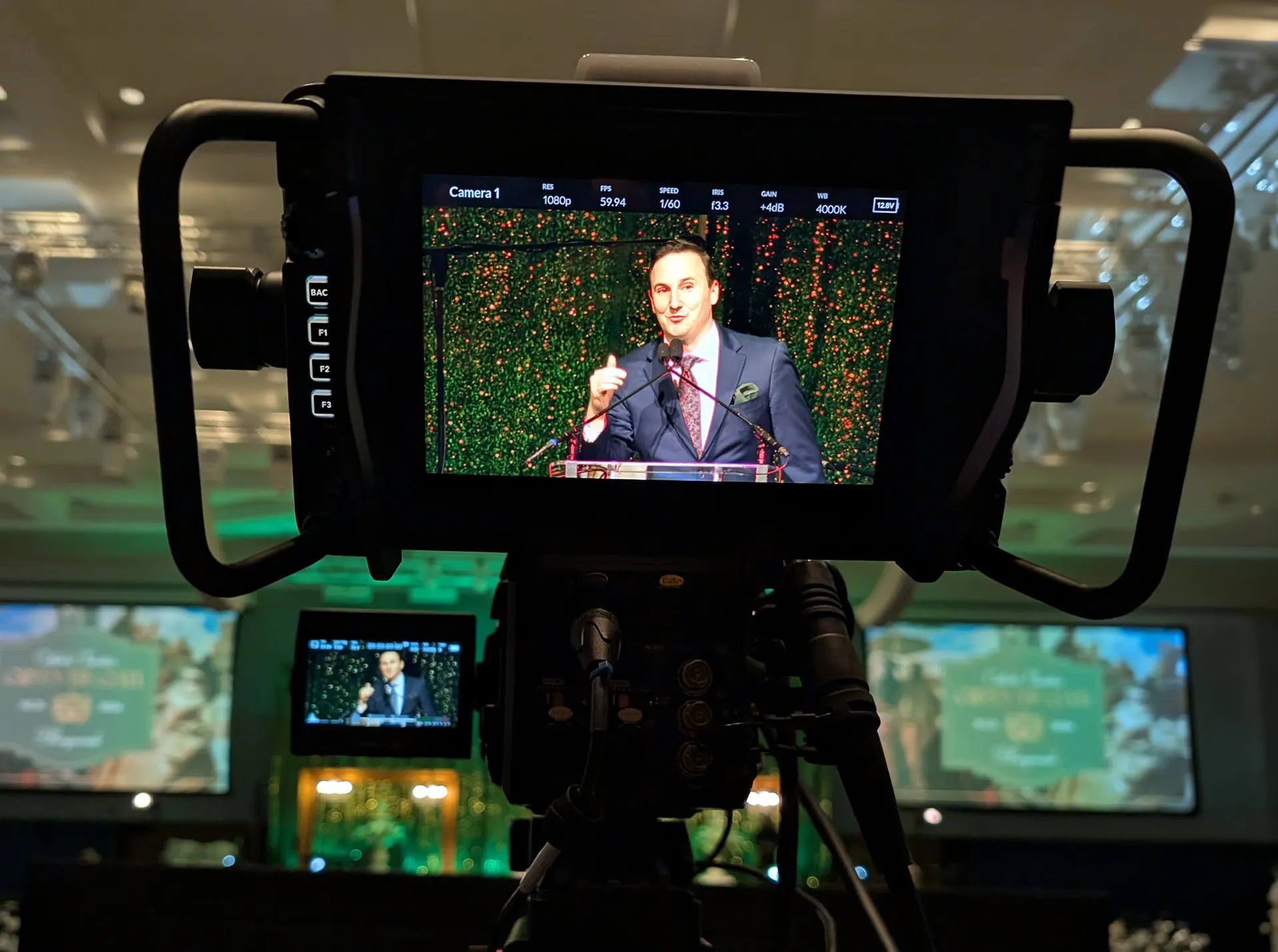 Camera monitor capturing a speaker at the podium during the Green Tie Gala, framed by a green sequin backdrop